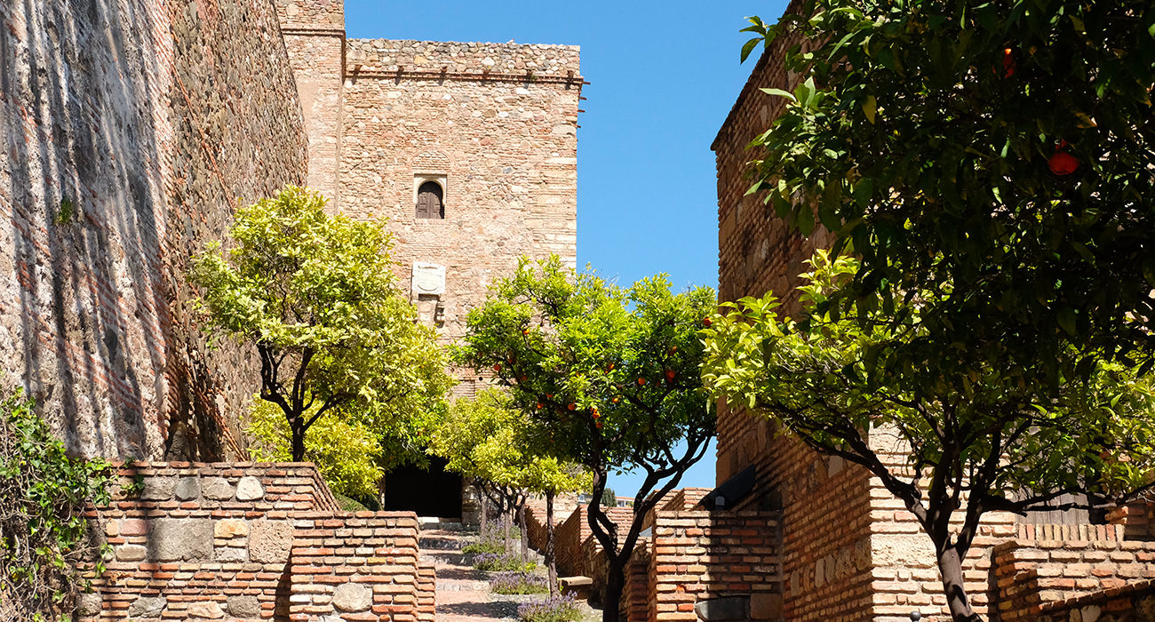 Photo de l'entrée du chateau en pierres de l'alcabaza de Malaga avec des orangers 