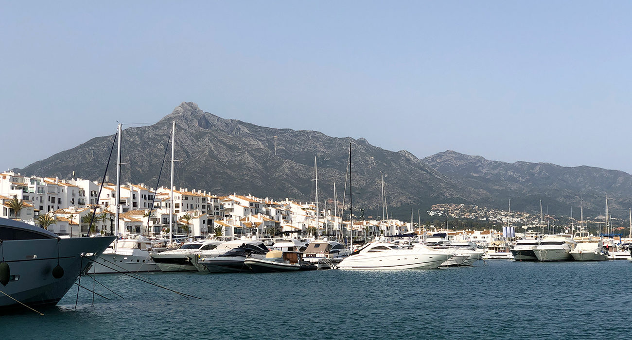 Photo du port avec les bateaux de Marbella, la ville derrière et la montagne dans le fond.